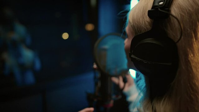 Blonde woman singing in professional recording studio, voice acting and podcast. Back view of talented singer or dubbing actress recording her voice in studio, female rap performer creating music hit