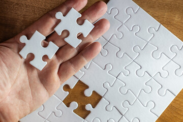 A hand holding two white puzzle pieces with one missing. Concept of completion and satisfaction, as the missing piece is the key to finishing the puzzle