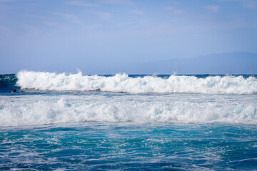 Waves coming ashore on a sunny day. Blue wave wall with white foam coming ashore where surfers surf. Atlantic Ocean. Tenerife, Canary Islands, Spain.