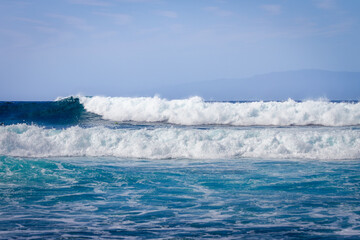 Waves coming ashore on a sunny day. Blue wave wall with white foam coming ashore where surfers surf. Atlantic Ocean. Tenerife, Canary Islands, Spain.