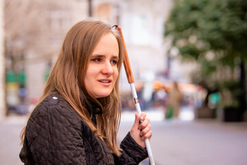 A visually impaired woman holding a white cane and standing in the city