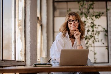 A woman with blond hair sitting at desk and using her laptop at home