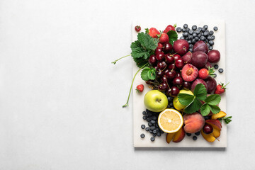 Set of summer ripe berries and fruits on a marble board, top view with copy space. Cherry, strawberry, blueberry, apples, lemon, plum, peach on a light background