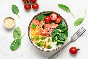 Salmon bowl with spinach, rice, avocado, tomato, cucumbers on a white background, top view. Poke bowl, healthy eating
