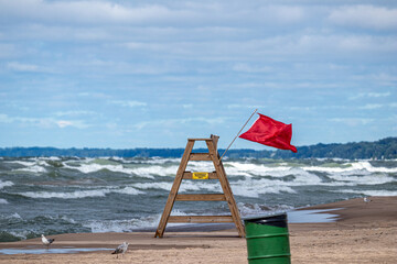 lifeguard chair on the beach with red warning flag flying due to hazardous water conditions 