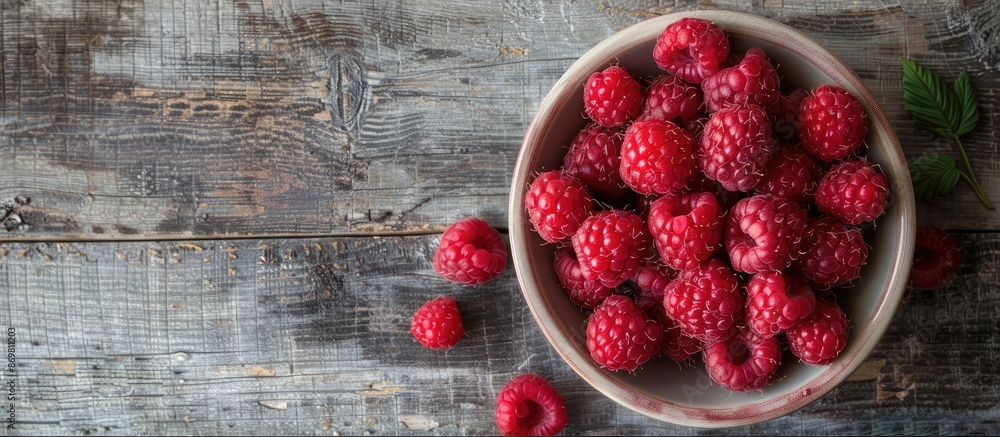 Aufkleber red raspberries arranged in a bowl against a grey wooden backdrop, leaving room for a copy space ima