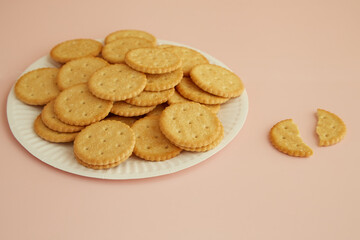 Crackers on a disposable plate and one cookie broken in half on a pink background, freshly baked cookies, tender cookies..