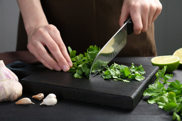 Woman cutting fresh coriander at black wooden table, closeup