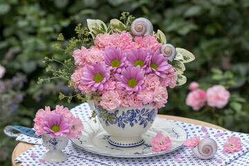 romantisches Blumen-Arrangement mit pink Rosen und Chrysanthemen in einer Tasse im Garten