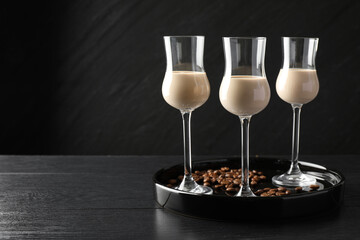 Coffee cream liqueur in glasses and beans on black wooden table, space for text
