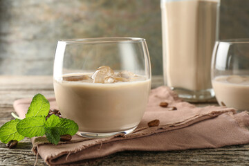 Coffee cream liqueur in glass, mint and beans on wooden table, closeup