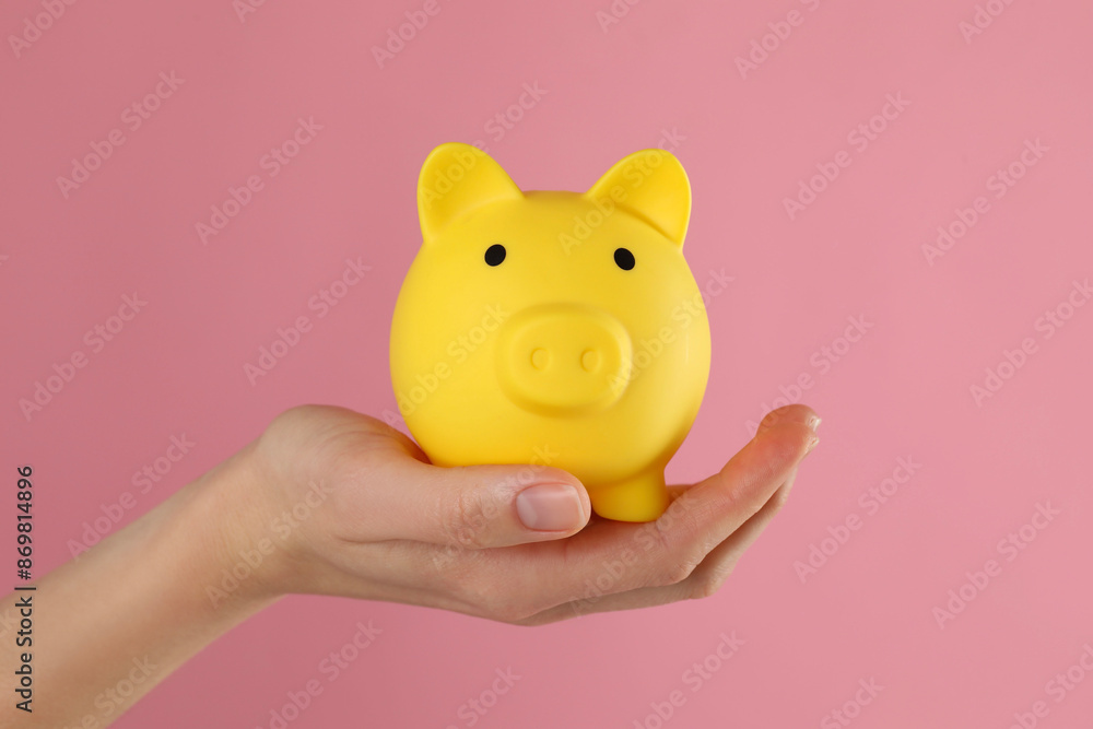 Wall mural woman with yellow piggy bank on pink background, closeup