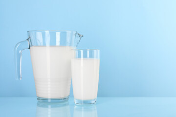 Jug and glass of fresh milk on light blue background, space for text