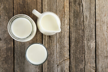 Jug of fresh milk, glass and carafe on wooden table, flat lay. Space for text
