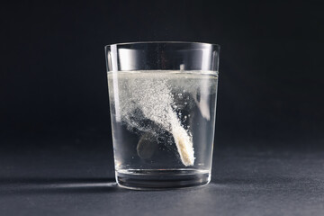 Effervescent pill dissolving in glass of water on grey table