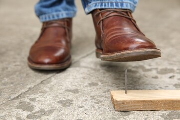 Careless man stepping on nail in wooden plank outdoors, closeup