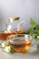 Aromatic jasmine tea in cups, flowers and green leaves on light grey table