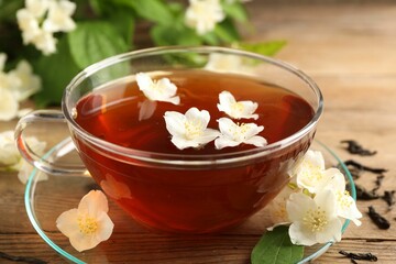 Hot jasmine tea in cup and flowers on wooden table, closeup
