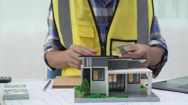 Professional architect team and engineer discuss about architectural project on meeting table with safety helmet, wooden block and architectural document scatter around. Closeup. Delineation.