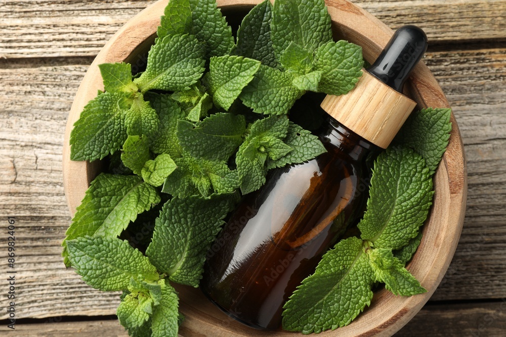 Wall mural Bottle of mint essential oil and fresh leaves on wooden table, top view