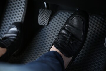 Man in black shoes pushing on pedal of car brake, closeup
