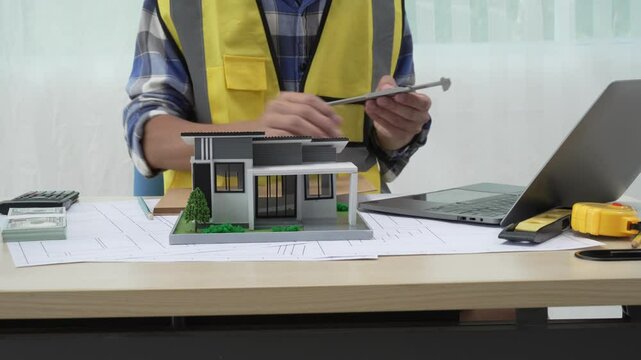 Professional architect team and engineer discuss about architectural project on meeting table with safety helmet, wooden block and architectural document scatter around. Closeup. Delineation.