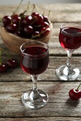Delicious cherry liqueur in glasses and fresh berries on wooden table