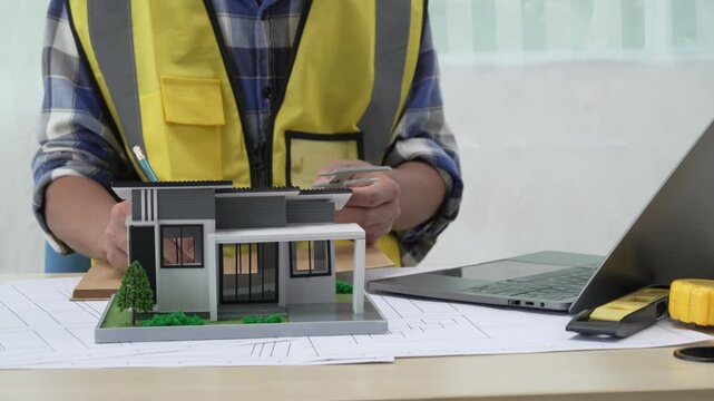Professional architect team and engineer discuss about architectural project on meeting table with safety helmet, wooden block and architectural document scatter around. Closeup. Delineation.