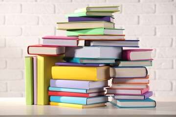 Stacks of many colorful books on white wooden table against brick wall
