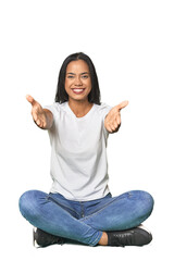 Latina sitting on floor in studio showing a welcome expression.