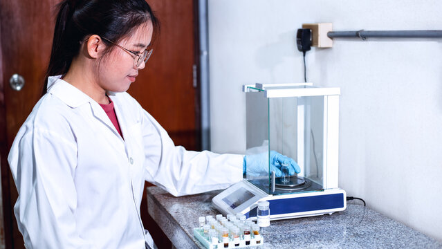 A scientist in a white lab coat and blue gloves is using an analytical balance 4 digits precision to weigh a clear vial for weighing a sample used in laboratory, scientific, scientific research.