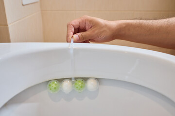 Gently placing a toilet bowl cleaning tablet containing floating balls with your hand