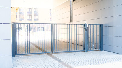 A metal gate with a black background. The gate is open and there is a parking lot in the background.