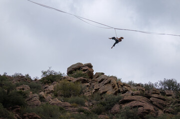 A person is balancing on a tightrope stretched between rocky cliffs.
