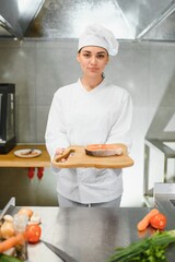 young beautiful female chef cooks salmon in restaurant kitchen