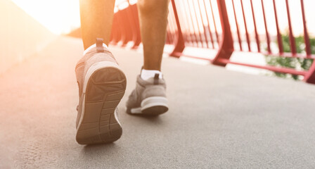 A close-up shot of a persons feet walking on a bridge, with the sun shining brightly in the background.