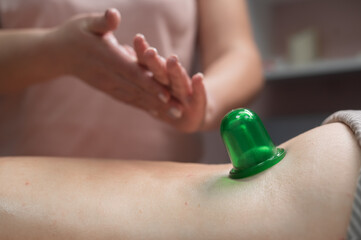 A woman undergoes an anti-cellulite massage procedure using a vacuum jar. Close-up of the lower...