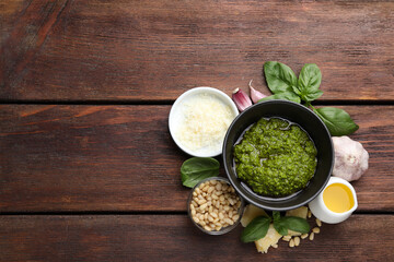 Tasty pesto sauce in bowl, basil, pine nuts, cheese, garlic and oil on wooden table, top view....