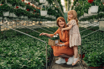 Happy mother and daughter florist with basket of flowers at hothouse