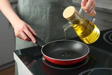 Vegetable fats. Woman pouring oil into frying pan on cooktop in kitchen, closeup