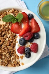 Tasty granola with berries and yogurt in bowl on light blue wooden table, flat lay