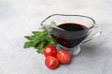 Balsamic vinegar in gravy boat, tomatoes, parsley and dill on gray textured table