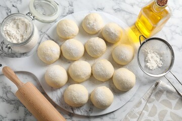 Raw dough balls, flour, rolling pin and oil on white marble table, top view