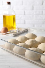 Raw dough balls in baking dish, egg and oil on white wooden table