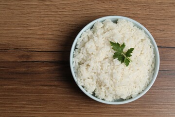 Tasty cooked rice with parsley in bowl on wooden table, top view. Space for text