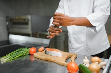 African American male chef preparing salmon fish in restaurant kitchen