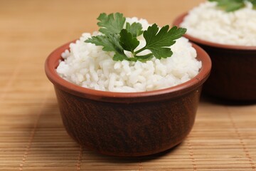 Bowls of delicious boiled rice with parsley on bamboo mat, closeup