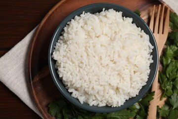 Delicious boiled rice served with parsley on wooden table, top view