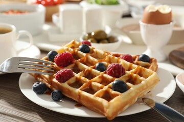 Tasty breakfast. Belgian waffles with berries, caramel sauce and cutlery on wooden table