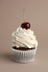 Delicious cupcake with cream and cherry on dark beige background